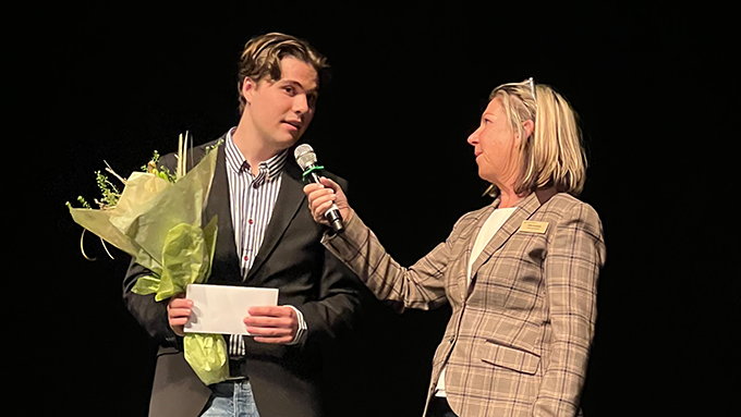 Bild på två personer i intervjusituation på en scen med svart bakgrund. En person har mikrofon. Den andra håller i en blombukett.