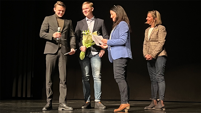 Bild på fyra personer i en intervjusituation på en scen med svart bakgrund. En person håller i en mikrofon. En annan person håller i en blombukett.